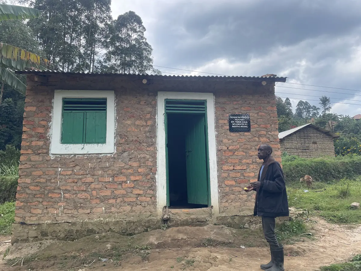 Small brick house with a green door and metal roof in a Batwa community