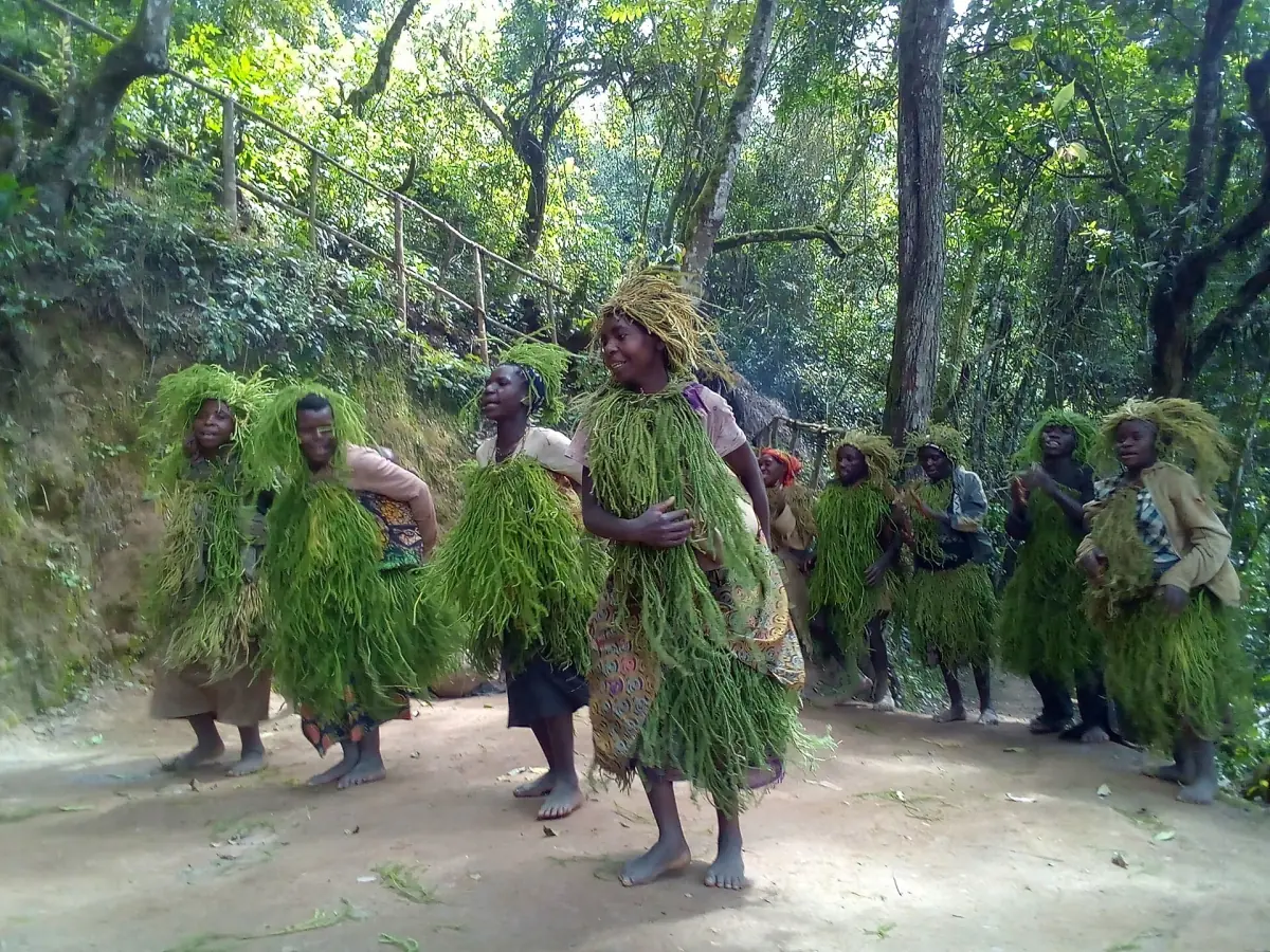 Group in grass costumes performing a cultural dance on a forest slope