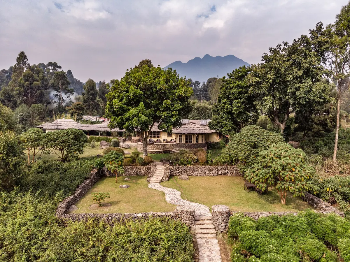 Garden and thatched lodge buildings below a volcano peak among trees