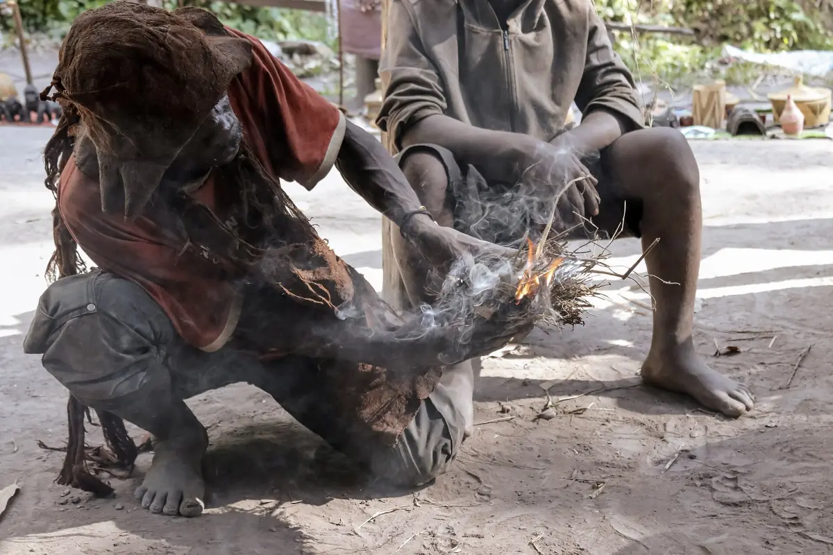 Man crouching over smoke while demonstrating traditional fire making